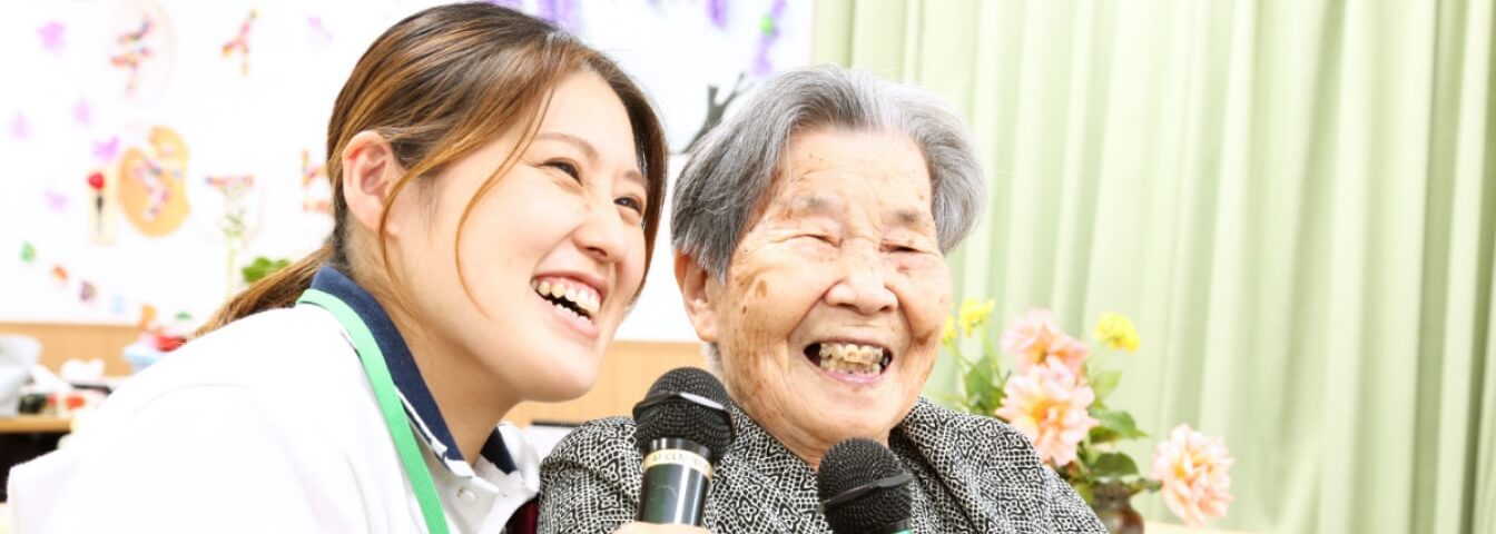 ご利用者さまと笑顔でカラオケを楽しむイズミの介護施設のスタッフ